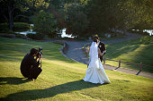 A man taking a photo of a bride and groom missing in grass