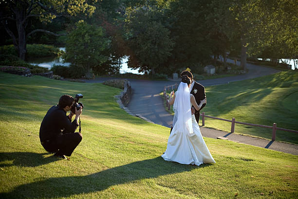 A man taking a photo of a bride and groom missing in grass stock photo
