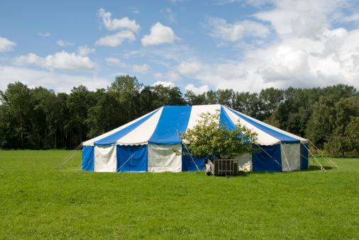 Striped blue and white party tent set up in a green meadow ready for a garden party.