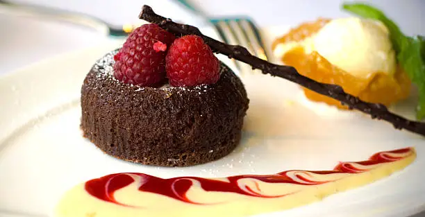 A chocolate lava cake dessert topped with fresh raspberries, vanilla ice cream in a tuile cookie, alongside creme anglaise and raspberry sauces. (SEE LIGHTBOXES BELOW for many more food photos...)