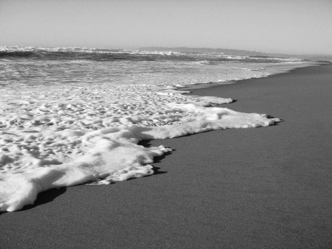 Black and white sunlit sea and beach scene.