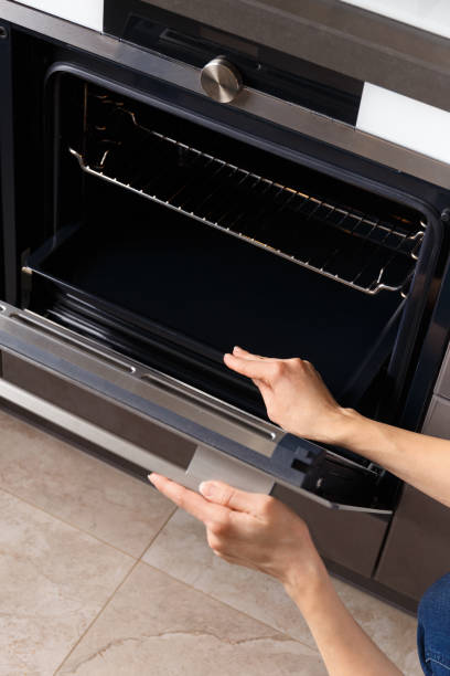 uma menina abre a porta de um forno embutido com uma exibição em um interior de cozinha moderna. - home interior women domestic kitchen cabinet - fotografias e filmes do acervo