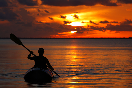 unrecognizable woman on kayak rowing at sunset in Florida Keys