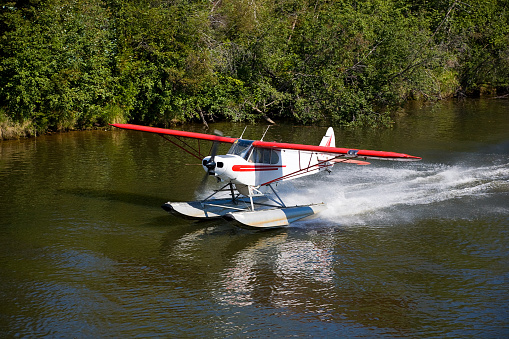 A small private float plane taking off in a wilderness setting.