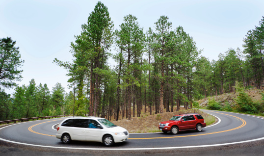 Tourists driving a red car and white sports utility vehicle or SUV around a hairpin curve on a winding road through a scenic forest near Mt. Rushmore National Monument in the Black Hills, South Dakota, USA. The area is a famous place and favorite travel destination for family road trips.