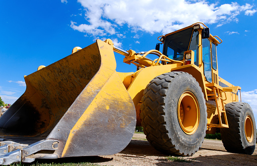 A yellow orange front end loader with a perfect blue sky background.