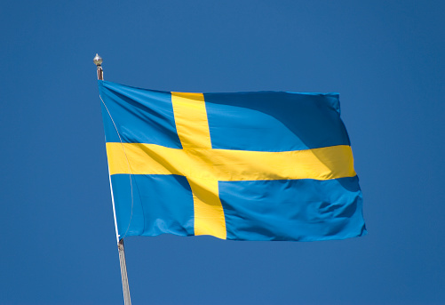 Sweden's flag blowing in the wind against a clear blue sky.