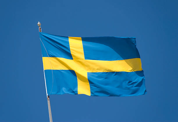 Swedish National Flag Sweden's flag blowing in the wind against a clear blue sky. sweden flag stock pictures, royalty-free photos & images