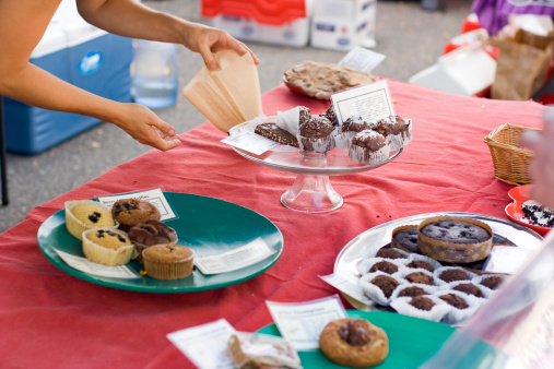 A woman holds open a pastry bag and presents the pastry choices to an unseen customer, at a weekend farmers market charity fundraiser bake sale.  Also take a look at these similar images: