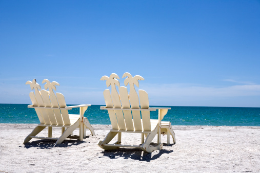 Back of two white wooden chairs on sand with ocean