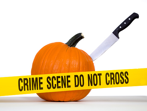 A pumpkin with a knife stabbed into it behind yellow \