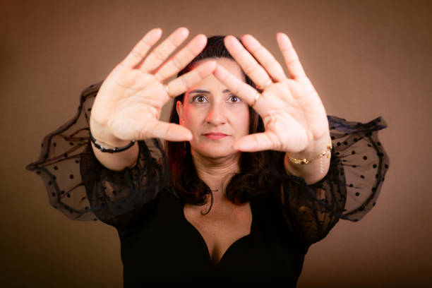 Coaching, beautiful woman in black clothing making forward hand gestures. Communicative and democratic management. Isolated on brown background.