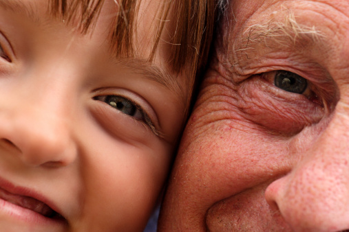 Close up detail of a young girl and her grandfather with their faces pressed close together.
