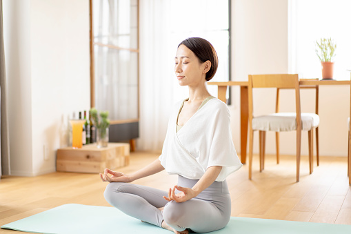 Asian woman is meditating in her living room at home.