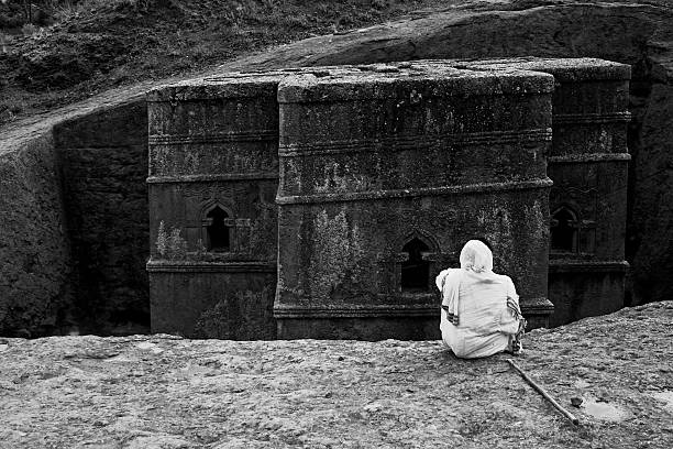 Priest praying in Lalibela B&W Bet Giorgis Bet Giorgis, Lalibela Ethiopia. Rock hewn church in Lalibela, Ethiopia. This church was built in the 12th century by hewing out all pieces of stone not needed. A praying priest is visible in the picture. black and white travel travel destinations monk stock pictures, royalty-free photos & images