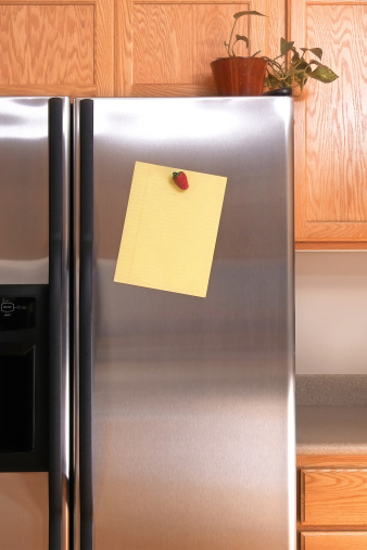 A piece of blank yellow note paper fastened to a refrigerator door with a strawberry magnet.