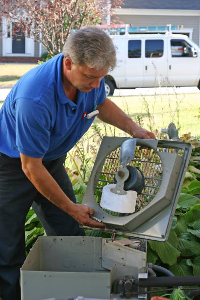 Man in blue shirt with gray hair repairing an AC outdoors stock photo