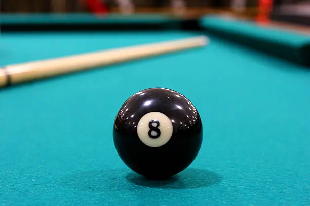 Eight ball on pool table with cue visible