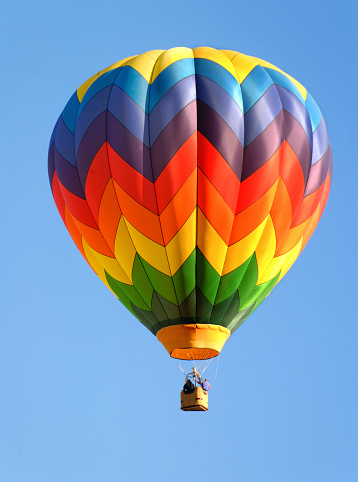 A colorful hot air balloon sails through a deep blue sky.