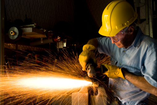 Industry:  Caucasian Man grinding in workshop.  He wears goggles, hard hat and gloves.  
