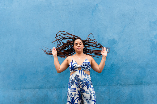 A pretty woman tossing her hair braids up against the blue wall of an old house. Pelourinho, Brazil.