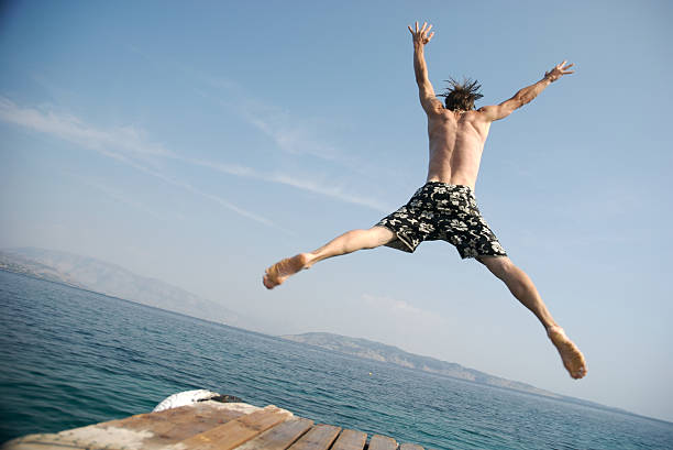 istock Young Man Jumping Off Pier Into Blue Water 157286535