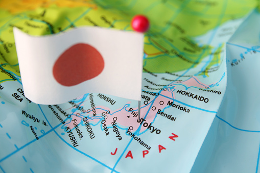 Japanese flag over cheap plastic map pointing Tokyo