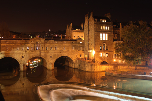 Pulteney Bridge in Bath, England.  A night time shot of the flowing River Avon, surrounded by limestone buildings and with the stars above.