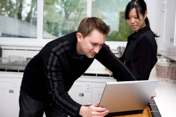 Asian and Caucasian Mixed Young Couple Using Laptop in Kitchen
