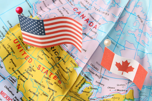 Closeup view of Canada and USA flags over cheap plastic map. Shallow depth of field