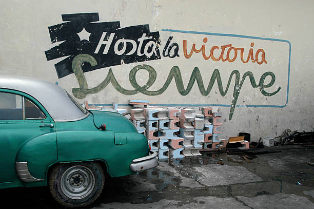 Classic car parked alongside fading Cuban revolutionary mural 
