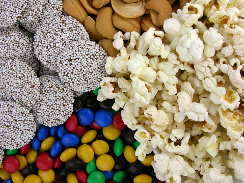 Host movie premieres with your buddies and delicious snacks. Side view photograph of tabletop featuring mouthwatering popcorn in striped boxes against red wall, providing space for movie advertisement