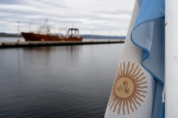 ARGENTINE FLAG IN THE PORT OF USHUAIA. BOAT MOORED IN THE PORT. TIERRA DEL FUEGO, ARGENTINE PATAGONIA.