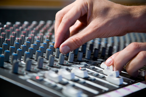 A pair of hands making adjustment on an audio soundboard.