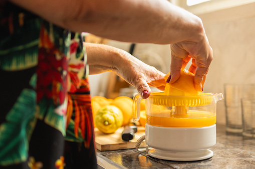 unrecognizable senior adult woman squeezing oranges in a juicer to make natural orange juice. concept drinking juices and eating fruit in summer.