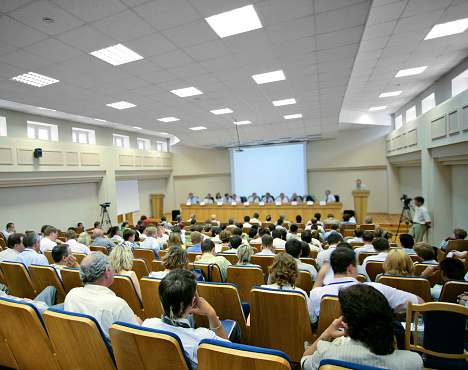 People sitting at a big conference hall during video-presentation. Focus on front.