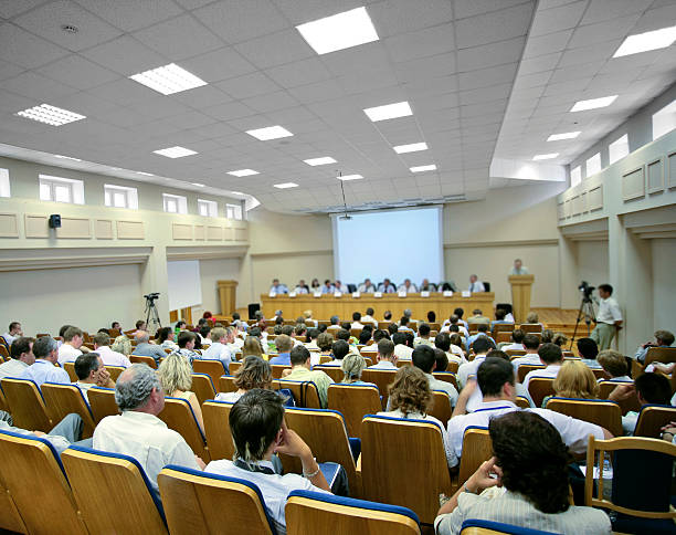 Video conference People sitting at a big conference hall during video-presentation. Focus on front. auditorium stock pictures, royalty-free photos & images