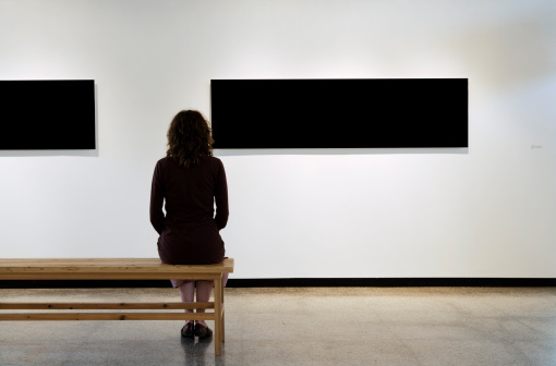 One woman seating on a bench and looking at two black frames in an art gallery. Concepts: art, museum; culture, space; room; exhibition.