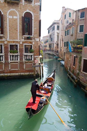 Venice, Veneto, Italy - Feb 19, 2023: A man taking photos of a beautiful blonde woman wearing a robe while rides on a gondola in Venice canals during 2023 carnival celebrations