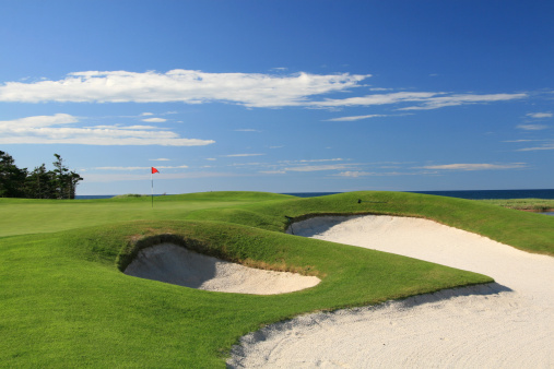 Beautiful white sand traps on a coastal course. PEI, Canada. Atlantic Ocean. Golf course scenic on a classic course in the maritime region of Canada. Nobody is in the image. Outstanding turf conditions and a red flagstick highlight the scene. Image taken during the summer on a postcard-perfect summer day. The golf industry is a major economic driver in Prince Edward Island. This course is located near Cavendish. 