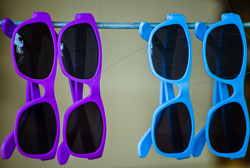 Purple and Blue fancy sunglasses hanging in the shop display, protective eyewear designed primarily to prevent bright sunlight.