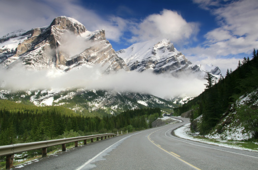 A scenic road in the mountains in winter with snow and ice. A stunning highway curls through the Canadian Rockies in Kananaskis Country near Calgary, Alberta. Nobody is in the image. Frosty and foggy early fall morning in one of the most beautiful parts of Canada. This is the Highwood Pass area.  