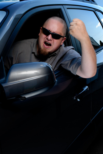 An angry driver shakes his fist out the window of his vehicle.