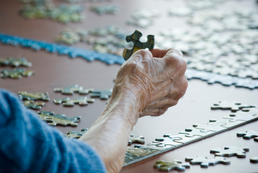An elderly lady passes the time by working on a jigsaw puzzle.
