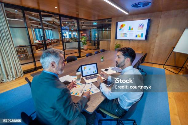 Two Business Men Meeting In A Board Room There Is Technology And Documents On The Conference Table Including A Laptop Stock Photo - Download Image Now