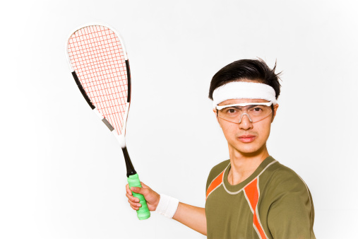 An Asian man holds a squash racquet, and looks intensely at the camera. He is a serious competitor, and is ready to take you on. The man is dressed in appropriate sports clothing.
