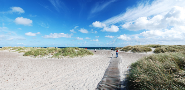 People walking towards water on boardwalk at a beach in Skagen, Denmark.