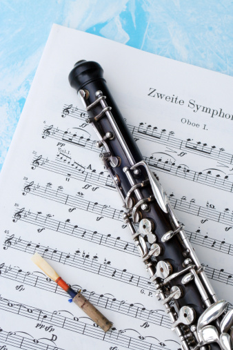 An oboe is lying on sheet music along with its reed.