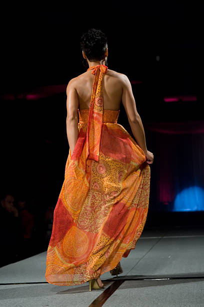 istock A brunette runway model in an orange dress from behind. 157295200