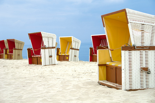 White wicker beach baskets chairs are standing on sandy beach, Baltic Sea, Hel, Poland. Interior of the baskets are yellow or red.